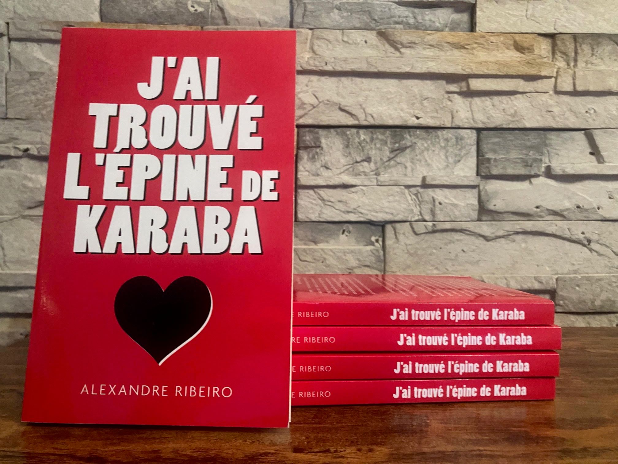 Exemplaires de J’ai trouvé l’épine de Karaba : un livre debout devant une pile de quatre, dos rouges visibles.